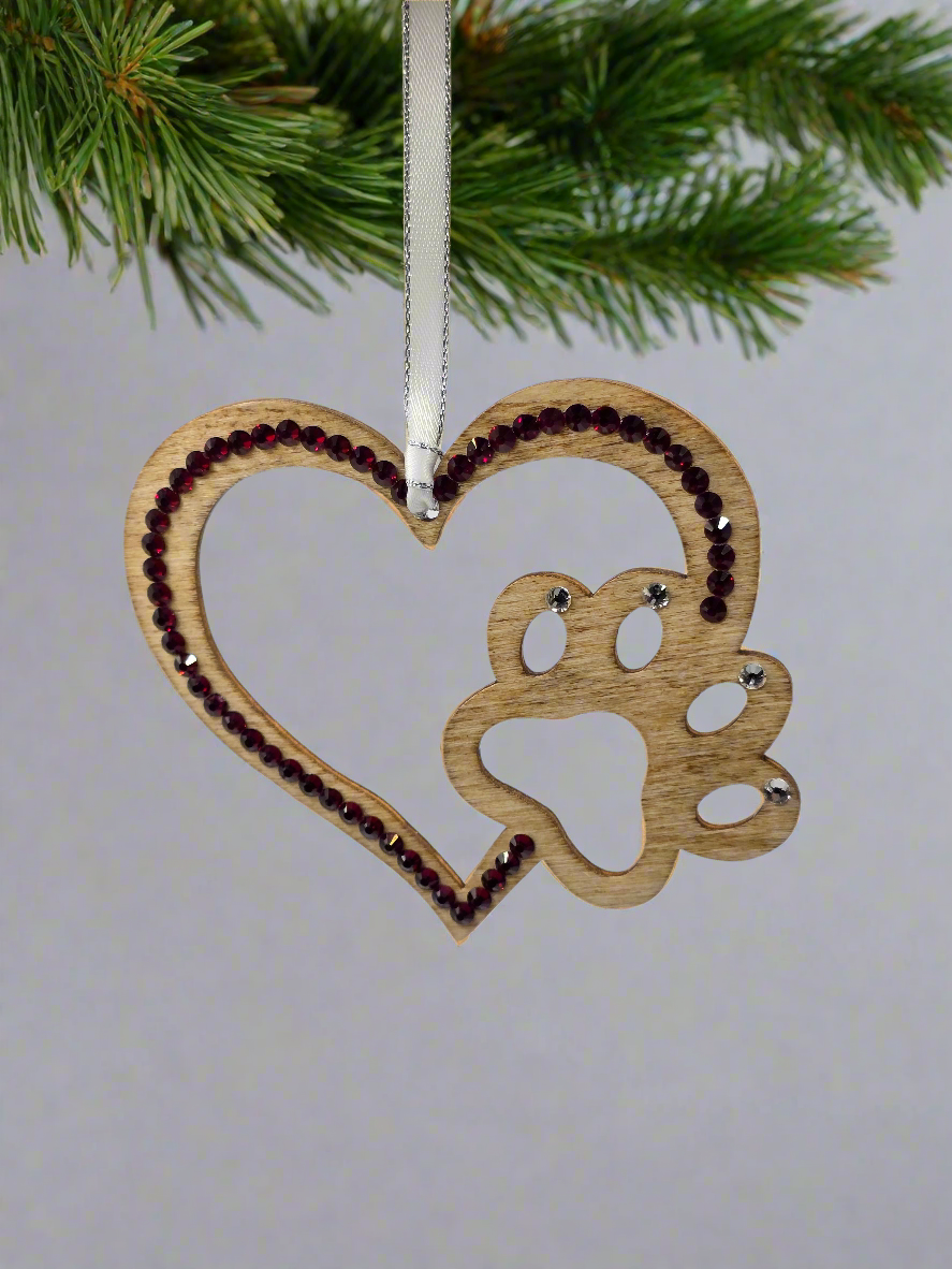 Wooden heart-shaped ornament with paw print design hanging on a Christmas tree.