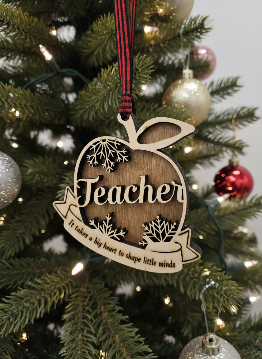 Wooden ornament shaped like an apple with 'Teacher' engraved, hanging on a decorated Christmas tree.